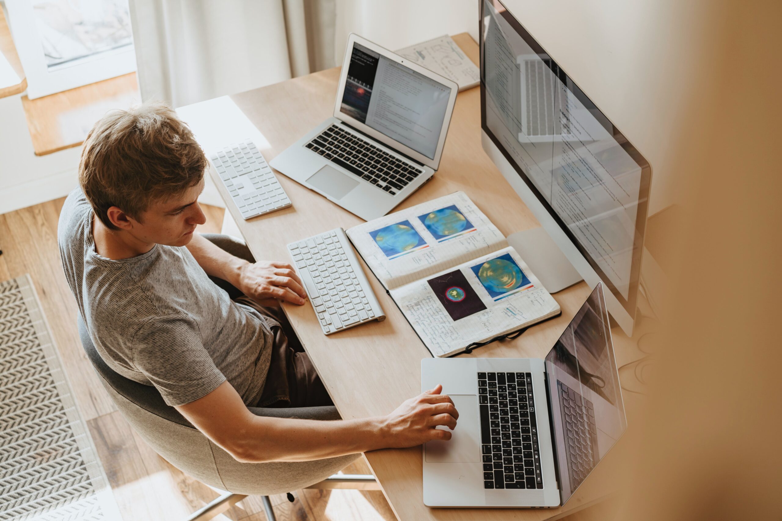 na imagem um homem sentando olhando para a tela de tres computadores ligados na sua frente passando a impressao de estar focado em seus estudos online ou trabalho